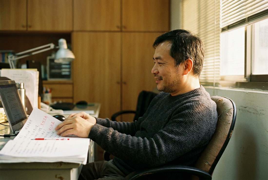 一位主管靠著椅背、神情放鬆地看著螢幕上一份成形的工作成果，桌上那份說明文件邊角有手寫補充的痕跡，暖光灑在桌面